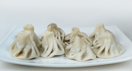 Boiled khinkalis with black pepper on a white porcelain plate