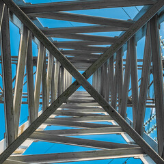 The metal tower structure of a high-voltage power lines from the inside, bottom view, against the blue sky