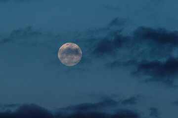 A full moon in a cloudy blue sky background