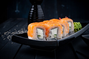 Philadelphia roll set with salmon, cucumber and cream cheese on a Japanese plate on a black wooden background with chopsticks and soy sauce