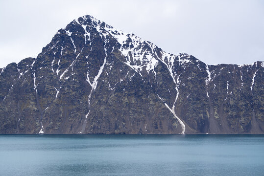 Snow covered mountain with blue water of a fjord on Spitsbergen
