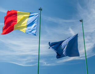 Romanian national flag an the flag of European Union waving against clear blue sky.