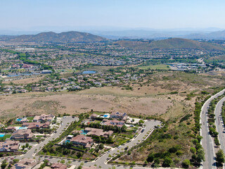 Aerial view of high class neighborhood with residential mansions and swimming pools in dry grass valley during hot summer. San Diego, California, USA.