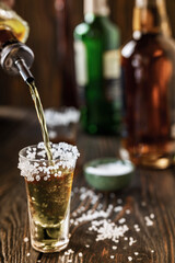 An alcoholic drink at the bar counter is poured into a tequila glass with salt at the edges, in the background are different bottles of alcohol, shallow depth of field, selective focus. The concept of
