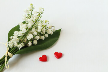Concept of Valentine's day celebration : two red hearts with a bouquet of fresh lilies of the valley on a white background, a place for the inscription