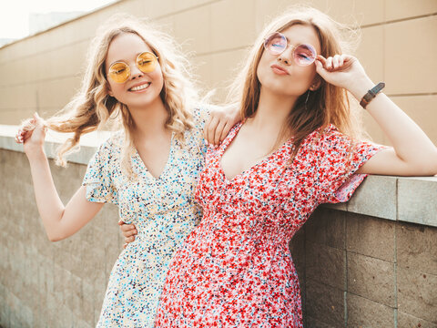 Two young beautiful smiling hipster girls in trendy summer sundress.Sexy carefree women posing on the street background in sunglasses. Positive models having fun and hugging