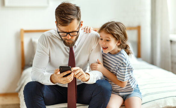 Busy father using smartphone near playful daughter.
