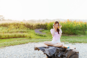 Asian cute girl wear pink shirt, white pants sitting on wood table listen song and work in garden at home.	
