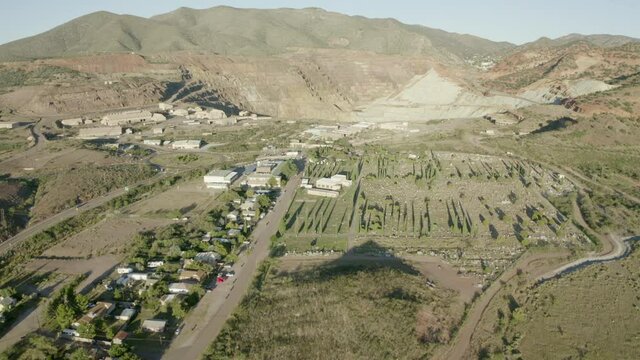 Aerial shot of houses in town near open-pit mine on sunny day, drone flying forward over residential structures against mountains - Bisbee, Arizona