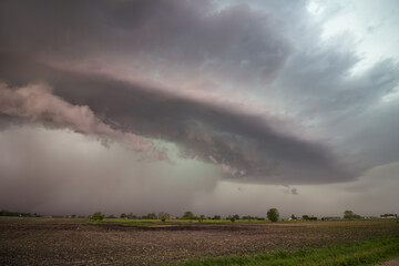 Fototapeta na wymiar A supercell thunderstorm hovers over a flat landscape, dropping rain and hail.