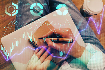 Double exposure of hands writing in notepad with stock market chart.