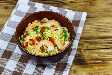 Bowl of instant Chinese noodles with shrimps, green onion and red hot chilli peppers on wooden table