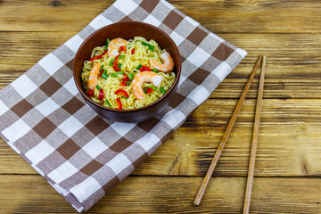 Bowl of instant Chinese noodles with shrimps, green onion and red hot chilli peppers on wooden table. Top view