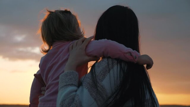 A young mother with a small child in the Park at sunset. The daughter puts her arms around her mother's neck. A happy family enjoys a beautiful sunset.