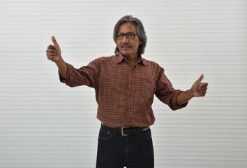 Naklejka premium Happy asian senior businessman in red casual shirt and blue jeans making thumbs up standing over white wall background, Business confident and success concept