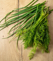 Green dill and onions on a wooden table.