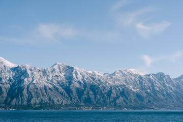 Fototapeta na wymiar Snow-capped mountain peaks in Kotor Bay, Montenegro, above the city of Dobrota. An assiable and fish farm in the sea.
