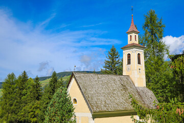 Fototapeta na wymiar Old church surrounded by fir trees on a background of mountains.