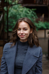 young happy smiling pretty girl in gray coat and turtleneck poses outdoors. Street style portrait...