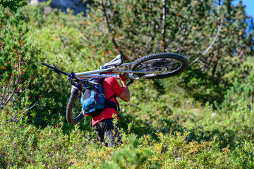 Mountainbiker trägt sein Rad auf einem unfahrbaren Pfad aufwärts