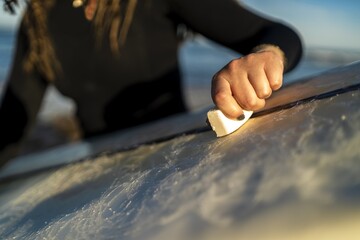 Selective focus shot of a female waxing her surfboard at the beach in Spain