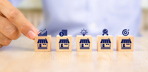 Close-up hand choose cube wooden toy blocks place in line up with franchise business store icon....