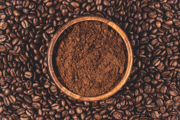 Wooden bowl filled with ground coffees on the coffee beans surface.