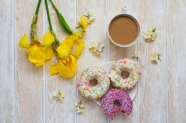 Cozy breakfast flat lay top view. Doughnuts and coffee with milk and yellow irises. Nice coffee break and good morning