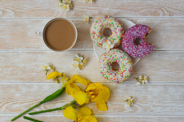 Cozy breakfast flat lay top view. Doughnuts and coffee with milk and yellow irises. Nice coffee break and good morning