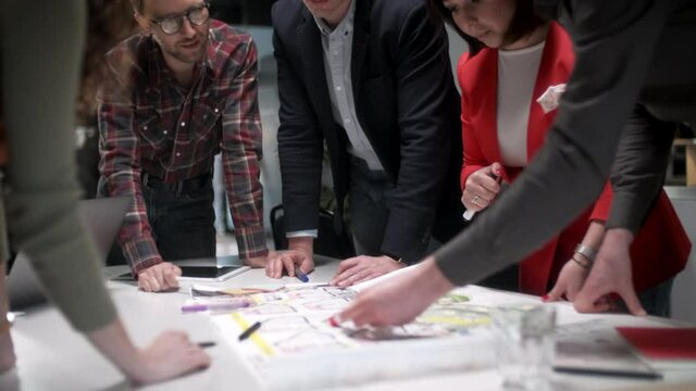 Team Of Architects Working On Project Paper Blueprint. Group Of Modern Business People In Casual Wear Discussing Architectural Designs While Sitting In The Creative Office.