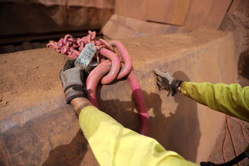 Trained crane rigger hand wearing a glove inspecting  crane lifting tag on the chain prior to use...