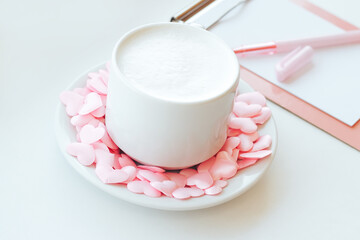Cappuccino cup decorated with pink hearts and tablet folder on white background