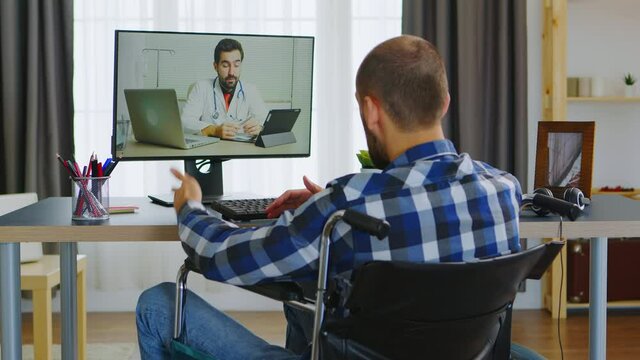 Young guy in wheelchair talking with his doctor about the process of rehabilitation on video call. Handicapped invalid paralysed freelancer, immobilized entrepreneur working from home, ilness