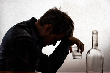 A silhouetted photo. A man in alcoholic intoxication holds a glass of alcohol. Alcoholism,...