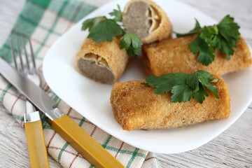 Croquettes with meat on white plate, one cut in half, decorated with green parsley, next cuttlery on table cloth, close up