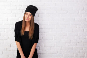 Portrait of young attractive cheerful girl wearing black clothes, studio shot over white bricks background.