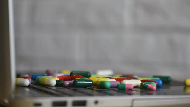 Colorful capsules, tablets falling onto the keyboard of the laptop. The concept of online shopping in a pharmacy.