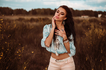 Dramatic portrait of a beautiful lady, outdoors, holding a mehendi drawing, bright makeup, bracelets, accessories, boho style, shirt, jeans