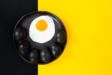 Black eggs on a black plate with a crashed egg on a flat black background with yellow, pop art.