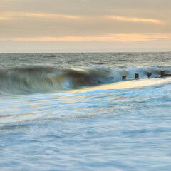 Abstract long exposure landscape image of waves crashing onto groynes on beach during sunset