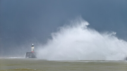 Fototapeta na wymiar Massive waves crash over harbour wall onto lighthouse during huge storm on English coastline in Newhaven, amazing images showing power of the ocean