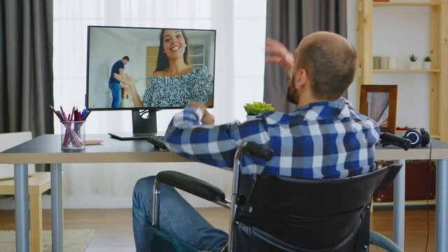 Guy in wheelchair because of walking handicap talking with his friends on video call. Handicapped invalid paralysed freelancer, immobilized entrepreneur working from home, ilness and disability
