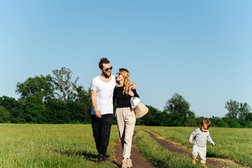 Spouses hug-walking in a countryside, their son running along.