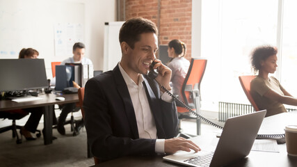 Smiling support service agent, employee consulting client on phone, using laptop, searching information, looking at computer screen, businessman holding phone negotiations, horizontal photo