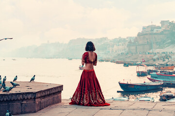 A beautiful Indian woman in a red Sari stands alone on the street. There is a flock of pigeons on...