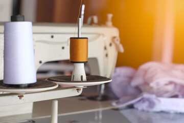 Brown and white thread roll of sewing machine for sew cloth or fabric with orange light close-up.
