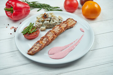Grilled pork medallions with pink sauce, potatoes and tomatoes with a white plate on a wooden background