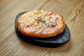 Delicious Georgian khachapuri - closed baked pie with homemade cheese on a wooden background