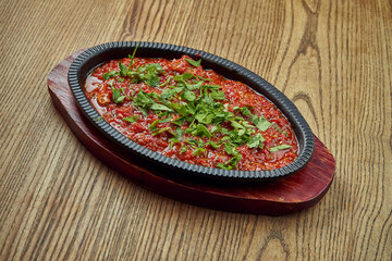 Chashushuli aromatic, spicy dish of meat (beef or veal), stewed in tomatoes in pan on wooden background. Georgian cuisine
