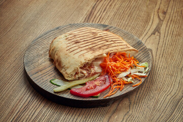 Yummy oriental shawarma with salad and sauce on a wooden tray against a wooden background. Kebab with meat or vegetables in pita